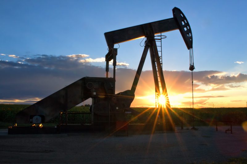 Pump Jack with the sun and setting in the background on a summer evening. The sunrays bursting through the oil rig