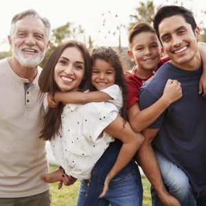 Three generation Hispanic family standing in the park, smiling to camera, selective focus
